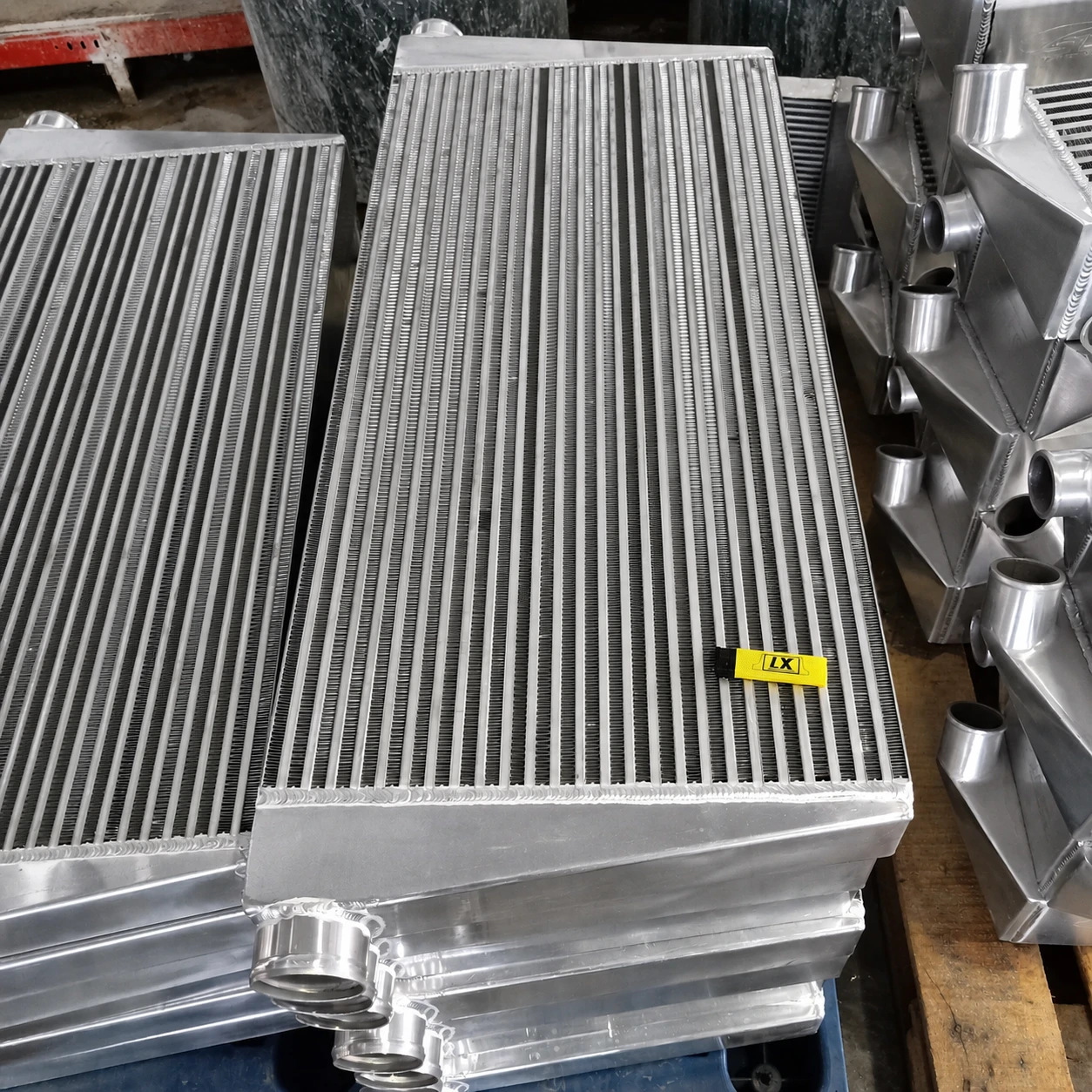 Large intercooler cores and aluminum end tanks arranged in a production batch, with an LX identification tag