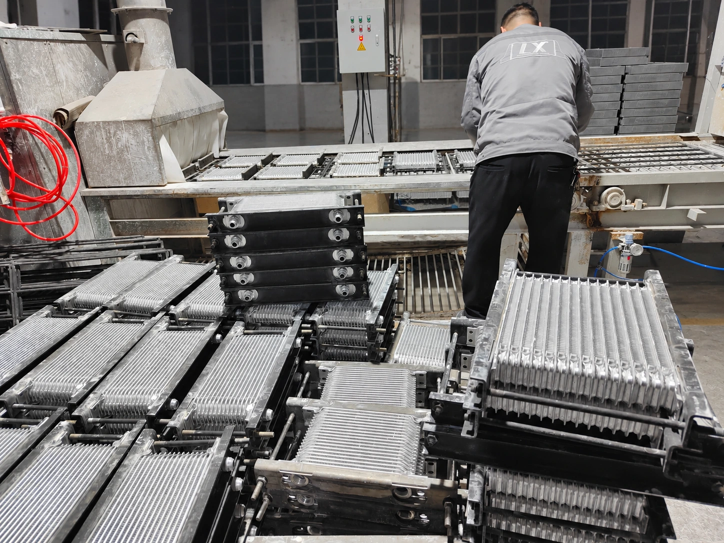 LX Performance operator handling oil cooler assemblies beside the brazing line