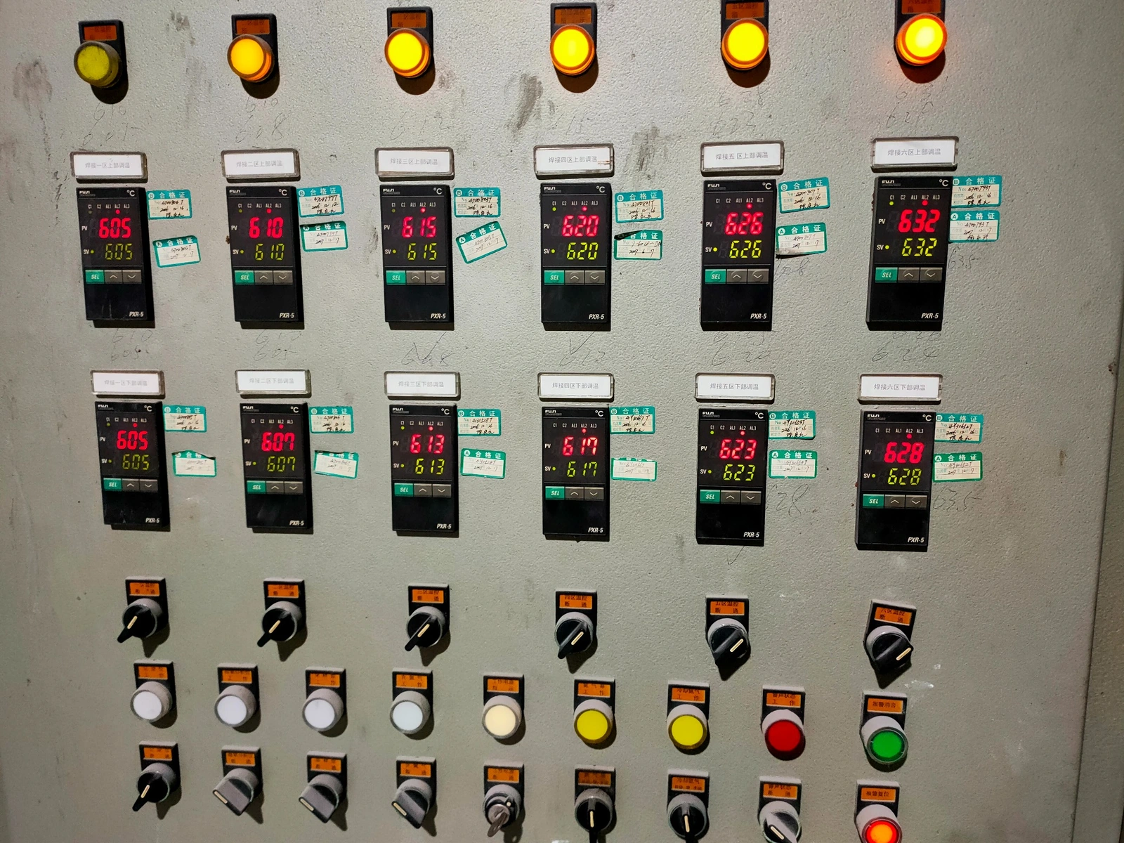 Close-up of twelve digital temperature controllers, indicator lamps and switches on the continuous brazing furnace control panel
