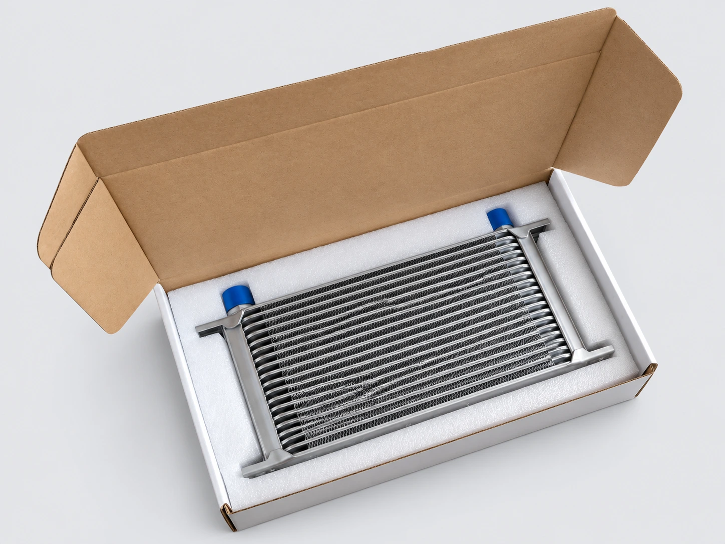 Oil cooler seated in a fitted white foam insert inside an individual cardboard carton, with blue port caps visible
